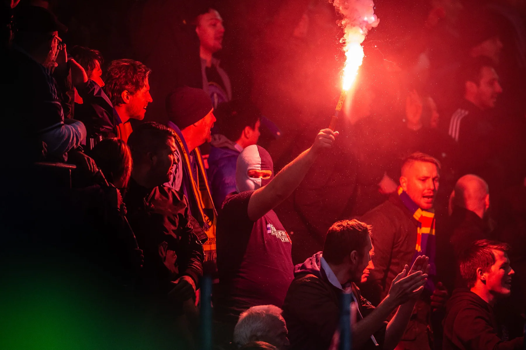 Supporter med bengal framför en röd läktare